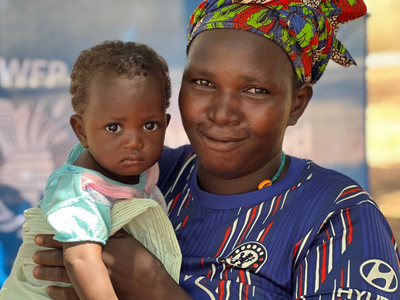 Photo: WFP/Myrline Sanogo-Mathieu A woman looks into the camera and smiles while holding a baby