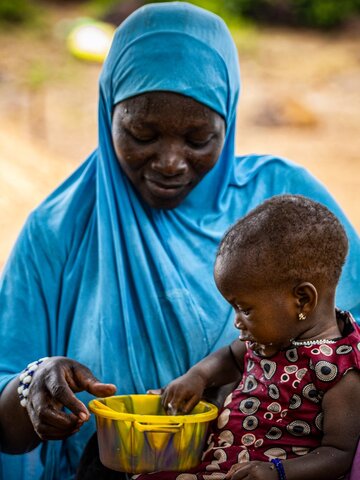A 10-month-old girl puts her hand in the plate containing the fortified porridge to drink it by hand.  © WFP/Cheick Omar Bandaogo