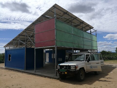 Partially built structure with colourful panels and a WFP vehicle in front, suggesting humanitarian aid in a rural or remote area.
