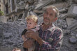 A late middle aged man holds up a small child against a background of rubble in Gaza