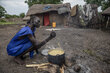 A woman in a blue dress stirs a pot of food cooking over a wood fire outside, with a mud and straw hut in the background. Photo: WFP/Gabriela Vivacqua