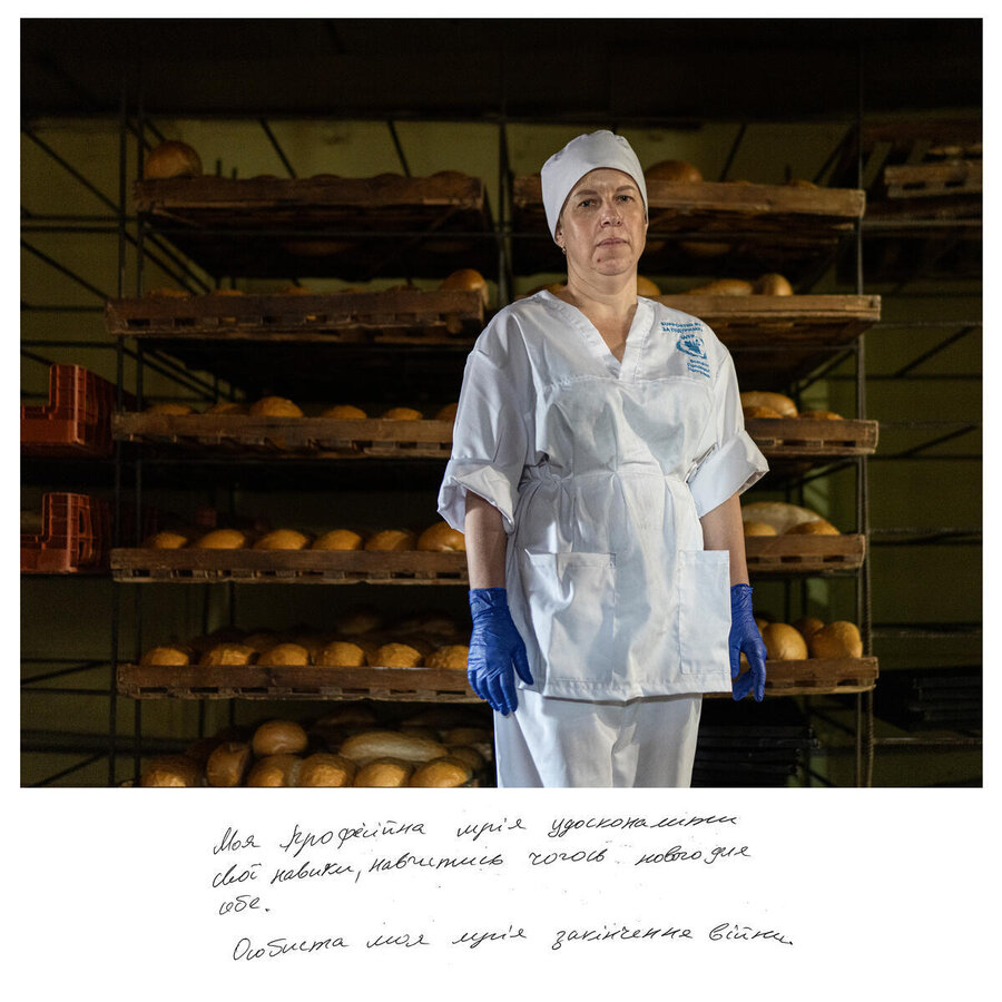 Ukranian woman in a white bakers' hat and outfit stands in front of rows of freshly baked bread