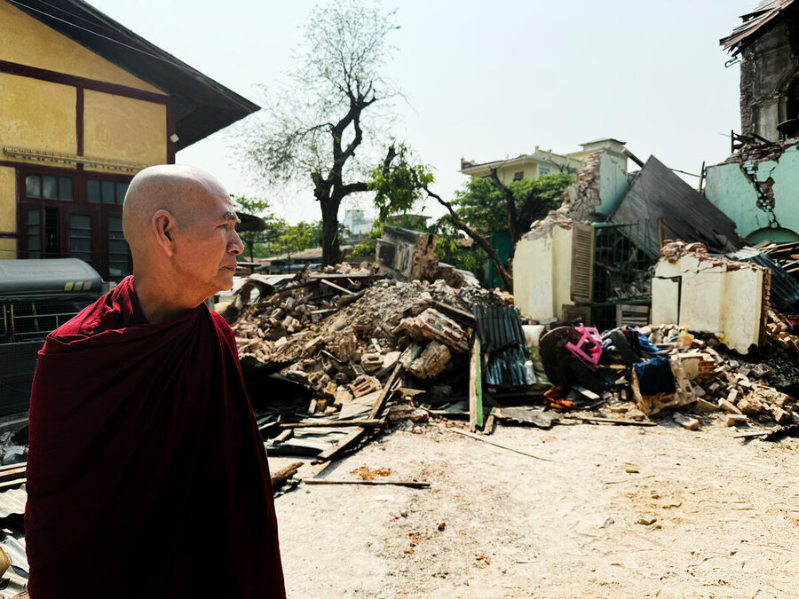 A monk looks contemplative standing in front of an earthquake damaged building