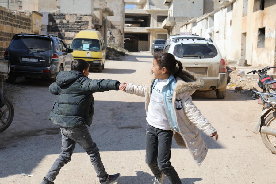 A girl and a boy wearing jackets swing around holding hands in sunny street in the middle east