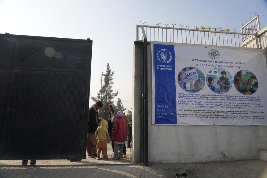 A family are dwarfed in between a huge iron sliding gate and a wall where a big WFP banner is draped