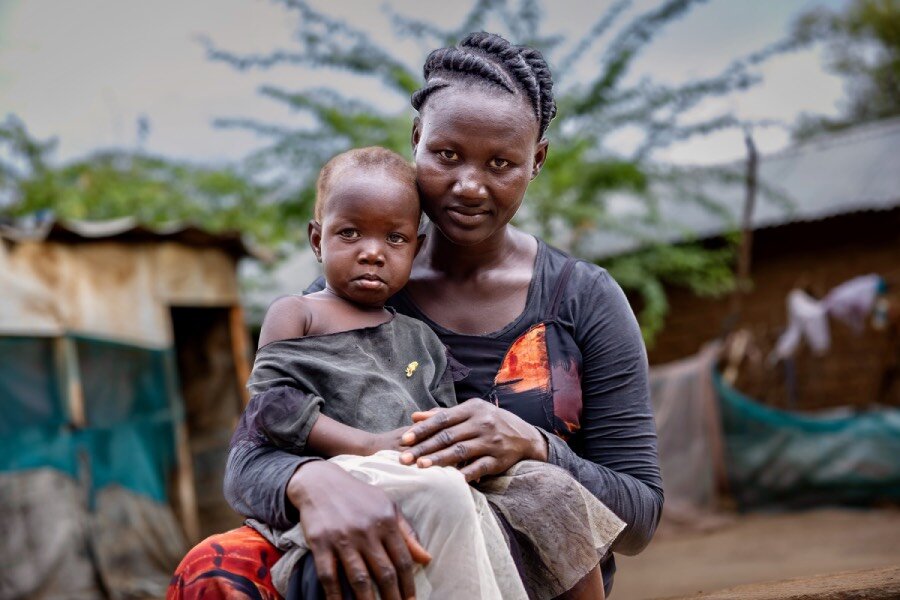 Refugee Waad holds one of her children as she stands next to blue-and-white tents at Kakuma refugee camp in Kenya. Photo: WFP/Dennis Matendechere