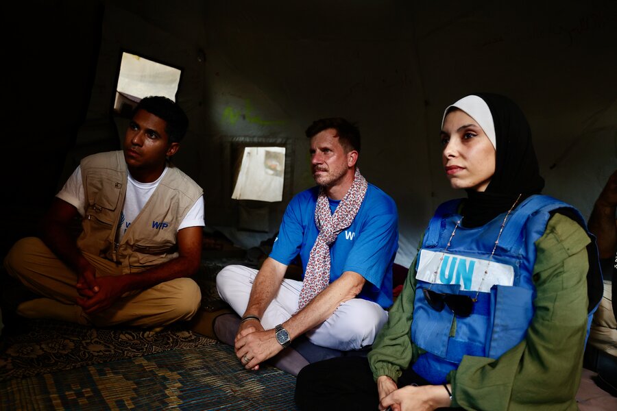 Three WFP employees sit in a dark tent speaking to a Gazan family (who are off camera). Photo: WFP/Ali Jadallah