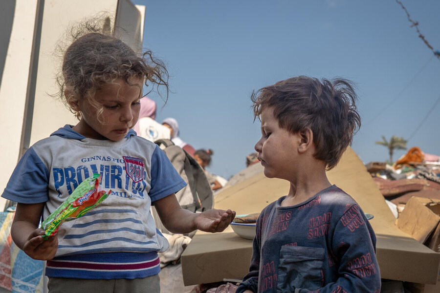 Girl and a boy in Gaza look dishevelled as they share something from a packet