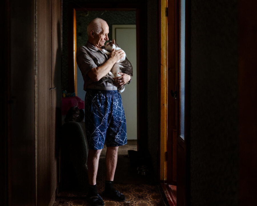 An old man strokes a cat he holds to his chest in a doorway