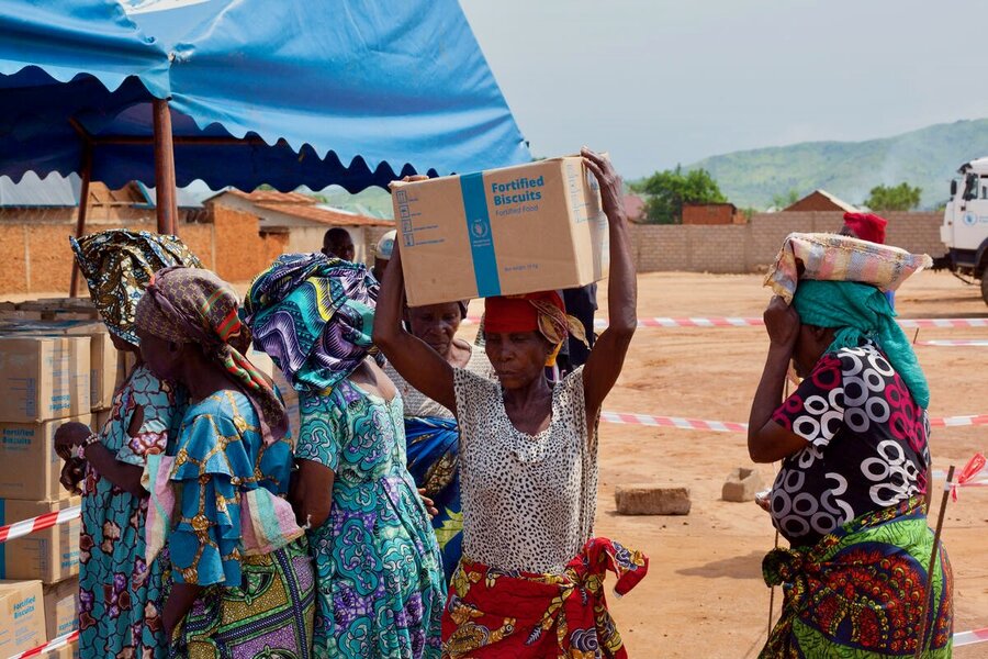 Women in colourful gowns pick up boxes of WFP food assistance being distributed from a blue tent in Sange, DRC. Photo: WFP/Musa Abema