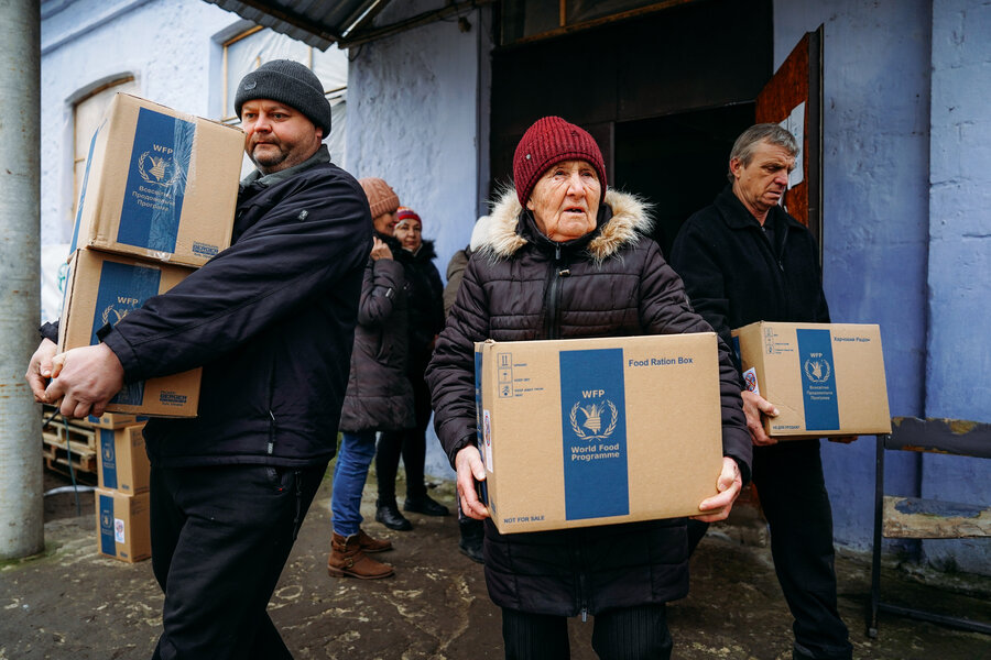 People carry WFP food boxes from a warehouse, distributing essential supplies to support families in need during cold weather.