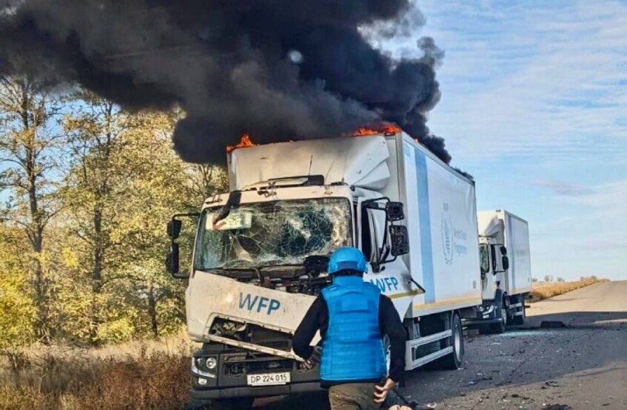 WFP security officer in a blue jacket and helmet investigates damaged truck with smoke billowing from its top. Photo: WFP