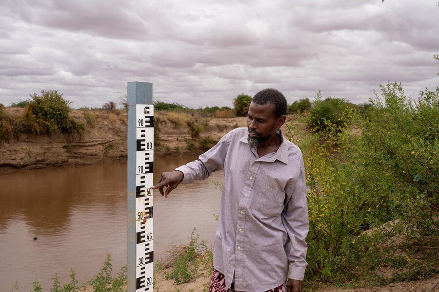 A man points to a measuring stick by a river that measures water levels. Photo: WFP/Sylve Njobati