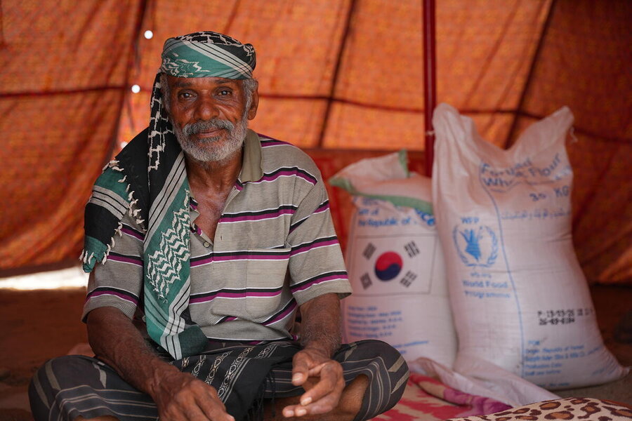 A man sits inside a tent beside sacks of WFP food assistance, including wheat flour, distributed to support families affected by crisis.