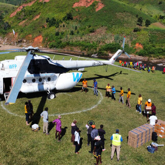 A WFP helicopter surrounded by WFP staff and beneficiaries in a field