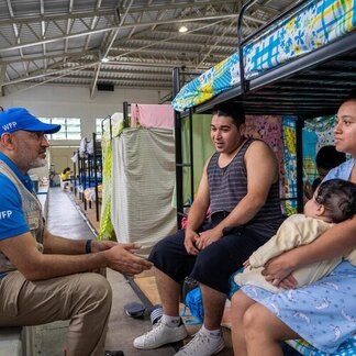 WFP staffer talking to man and woman with baby, inside a shelter